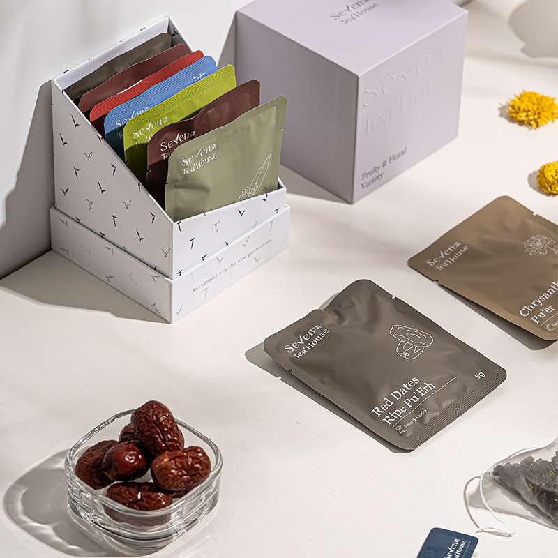 An open box of fruity and floral variety pack featuring the red dates ripe pu-erh tea bag on a white surface surrounded by red dates, yellow flowers, and a pyramid tea bag