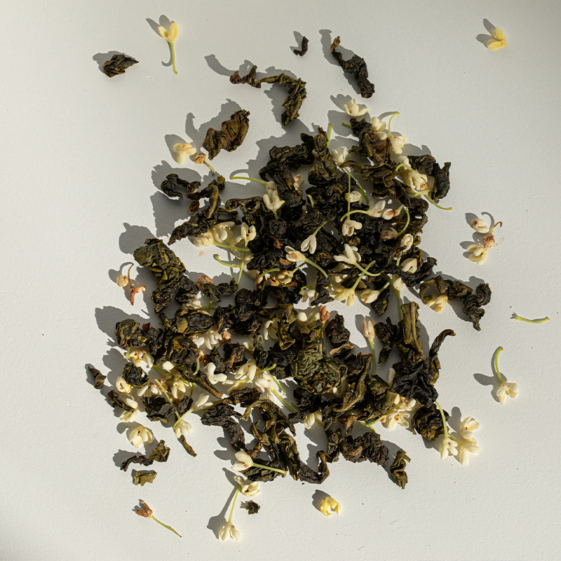 Osmanthus oolong tea leaves sprinkled with osmanthus flowers; shadows from the sun shining on the leaves and flowers