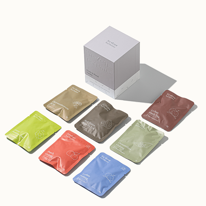 A variety of individually wrapped tea bags in a range of fruity and floral flavors, displayed in front of their packaging box labeled Seven TeaHouse