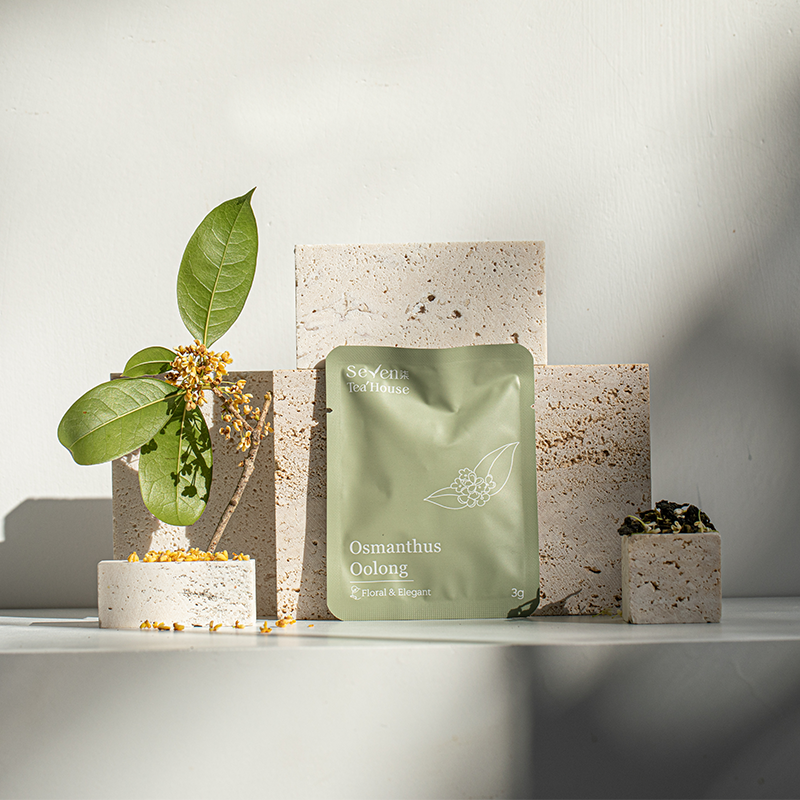 Elegantly display featuring a packaged osmanthus oolong tea bag (light green) with stone and floral elements