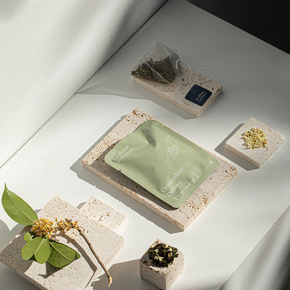 Green osmanthus oolong tea bags on stone tiles with decorative elements on a light surface