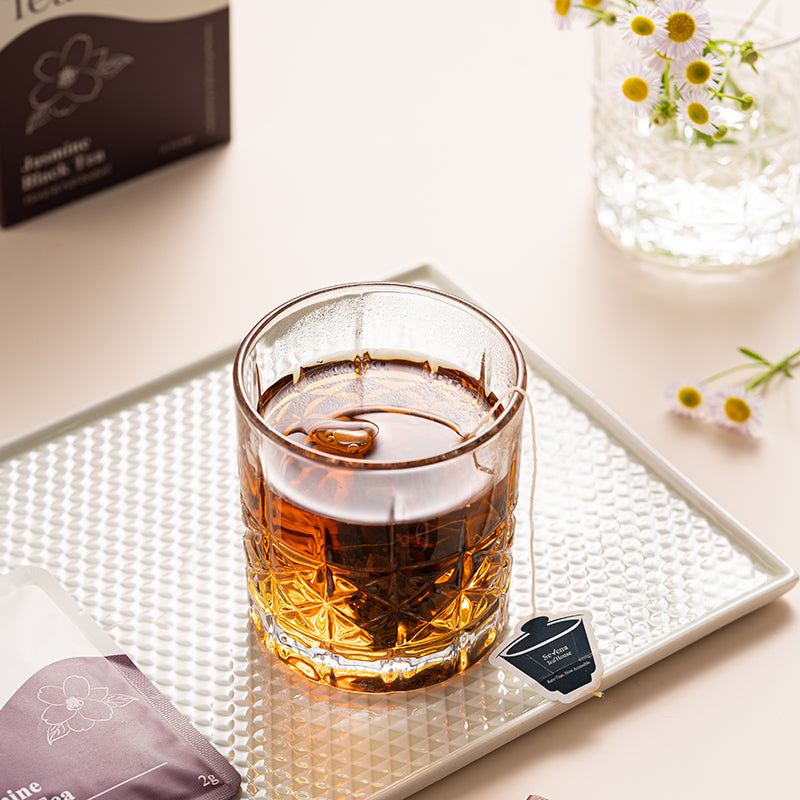Glass of tea on a textured tray with tea packaging and flowers in the background