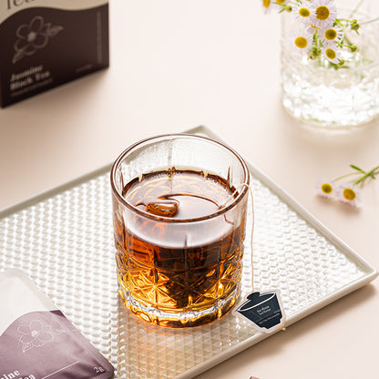 Glass of tea on a textured tray with tea packaging and flowers in the background